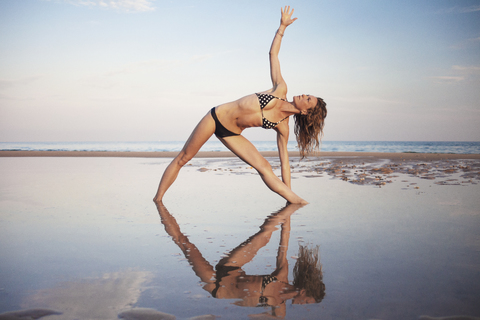 Frau im Bikini macht Yoga am Strand gegen den Himmel, lizenzfreies Stockfoto