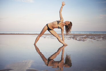 Frau im Bikini macht Yoga am Strand gegen den Himmel - CAVF23277