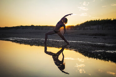 Woman wearing bikini practicing yoga at beach during sunset - CAVF23280