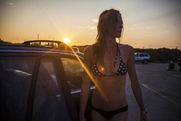 Woman wearing bikini standing by car during sunset - CAVF23282