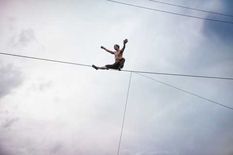 Niedriger Blickwinkel von Mann balanciert auf Seil während Slacklining gegen bewölkten Himmel, lizenzfreies Stockfoto