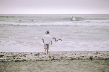 Rückansicht eines Jungen, der am Strand im Sand läuft - CAVF23333