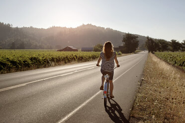 Rückansicht einer Radfahrerin auf der Straße inmitten eines Feldes - CAVF23370