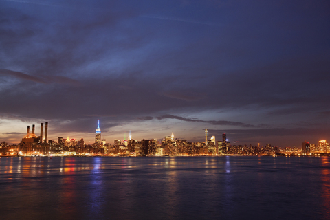 Scenic view of river and illuminated cityscape against cloudy sky at night stock photo