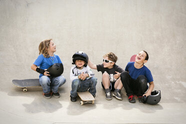 Fröhliche Jungen unterhalten sich, während sie auf einer Skateboard-Rampe sitzen - CAVF23422