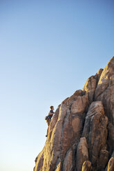 Low angle view of man climbing rock against clear blue sky - CAVF23445