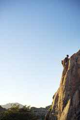 Low angle view of man climbing rock against clear blue sky during sunny day - CAVF23446