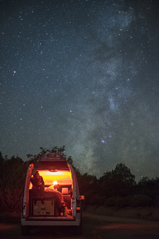 Man sitting in illuminated camper van against star field at night stock photo