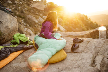 Frau im Schlafsack schaut weg, während sie sich auf einem Felsen entspannt - CAVF23450