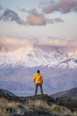 Rückansicht eines Wanderers mit Blick auf schneebedeckte Berge, lizenzfreies Stockfoto