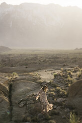 Junge Frau geht auf Felsen in einem Feld vor Bergen - CAVF23483