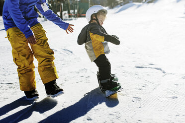 Hochformatige Ansicht des Vaters, der seine Tochter beim Snowboarden unterstützt - CAVF23499