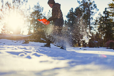 Niedriger Blickwinkel eines Mädchens, das mit einer Schaufel auf einem Feld Schnee entfernt - CAVF23504