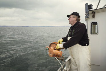 Seitenansicht eines Fischers, der auf einem Fischerboot vor einem bewölkten Himmel steht - CAVF23542