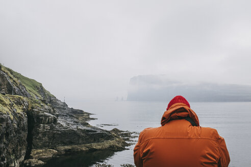 Rear view of hiker in hooded jacket against sea during foggy weather - CAVF23553