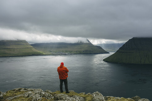 Hiker looking at view while standing on cliff against cloudy sky - CAVF23580