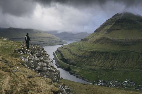 Wanderer mit Blick auf die Aussicht, während er auf einer Klippe gegen stürmische Wolken steht, lizenzfreies Stockfoto