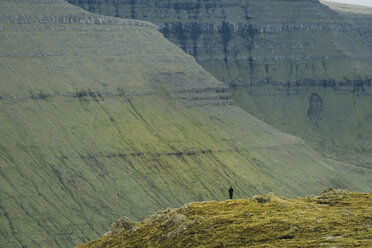Fernblick auf einen Wanderer, der auf einer Klippe in den Bergen steht - CAVF23611
