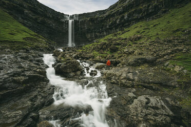 Distant view of hiker standing on rocks against waterfall - CAVF23620