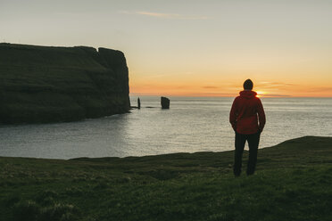 Wanderer, der bei Sonnenuntergang am Meer steht und die Aussicht betrachtet - CAVF23635