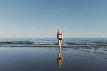 Rückansicht einer Frau, die einen Bikini trägt, während sie am Strand in Richtung Meer gegen den klaren Himmel läuft - CAVF23640