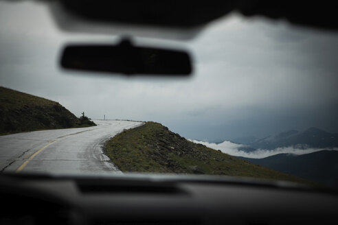 Country road by clouds covered mountains seen through car windshield - CAVF23651