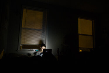 Woman using laptop computer in darkroom at home - CAVF23661