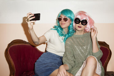 Women wearing sunglasses clicking selfie while sitting on couch against wall - CAVF23675