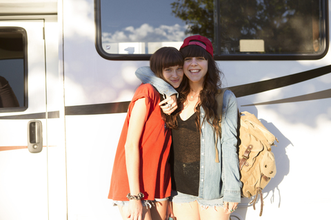 Glückliche junge Frauen auf einem Roadtrip, die zusammen vor einem Van stehen, lizenzfreies Stockfoto