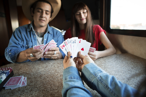 Ausgeschnittenes Bild einer Frau, die Karten hält, während sie mit Freunden im Wohnmobil spielt, lizenzfreies Stockfoto