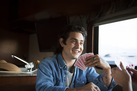 Glücklicher Mann, der mit seiner Freundin Karten spielt, während er im Wohnmobil sitzt, lizenzfreies Stockfoto