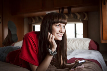 Thoughtful woman smiling while relaxing on bed in camper van - CAVF23701