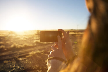 Frau fotografiert Feld mit Smartphone bei Sonnenuntergang - CAVF23710