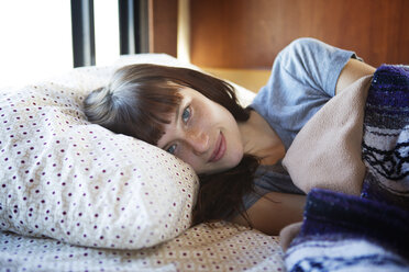 Portrait of woman lying on bed in camper van - CAVF23724