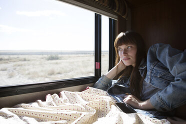 Woman looking out from window while lying on bed in camper van - CAVF23742