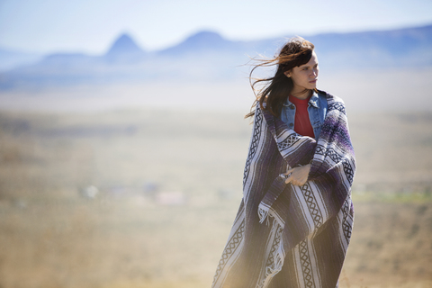 Nachdenkliche, in eine Decke gehüllte Frau auf einem Feld, lizenzfreies Stockfoto