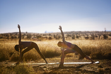 Freundinnen üben Yoga in Dreiecksposition auf einem Feld - CAVF23802