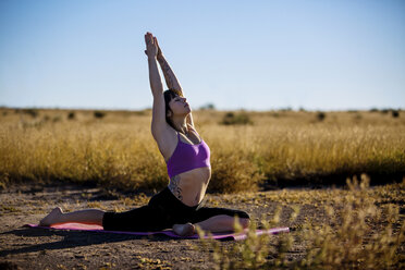 Junge Frau übt Yoga auf einem Feld - CAVF23804