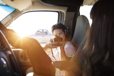 Man photographing woman through instant camera while sitting in camper van - CAVF23817