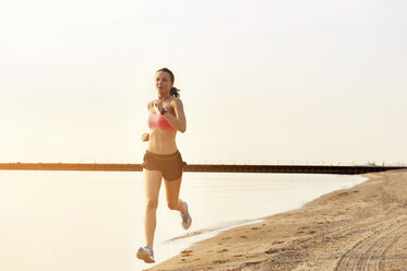 Weibliche Athletin joggt am Ufer gegen den klaren Himmel - CAVF23838