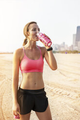 Female athlete drinking water while standing at beach - CAVF23839