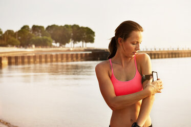 Weibliche Sportlerin beim Einstellen des Armbands am Strand - CAVF23841