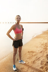 Female athlete listening music while standing on shore against sky - CAVF23843