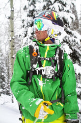 Man in ski-wear standing against tree - CAVF23856