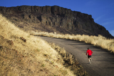 Rear view of man jogging on road by mountain - CAVF23870