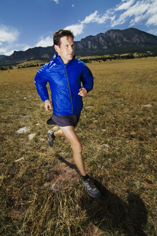 Mann joggt auf einer Wiese vor einem Berg, lizenzfreies Stockfoto