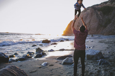 Rear view of playful father throwing son in air at beach - CAVF23887