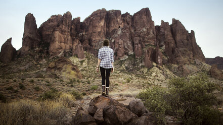 Rear view of Teenager standing on top of rocks against mountain - CAVF23928