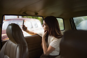 Teenager photographing through smart phone while sitting in car - CAVF23931