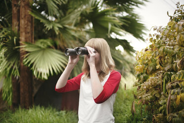 Teenager looking through binoculars while standing by plants at park - CAVF23936